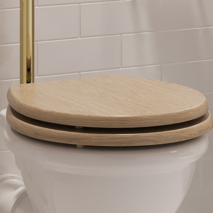 Product lifestyle image of Burlington Guild Light Oak Soft Close Toilet Seat with gold pipe and white metro tiled background GU6105LOK